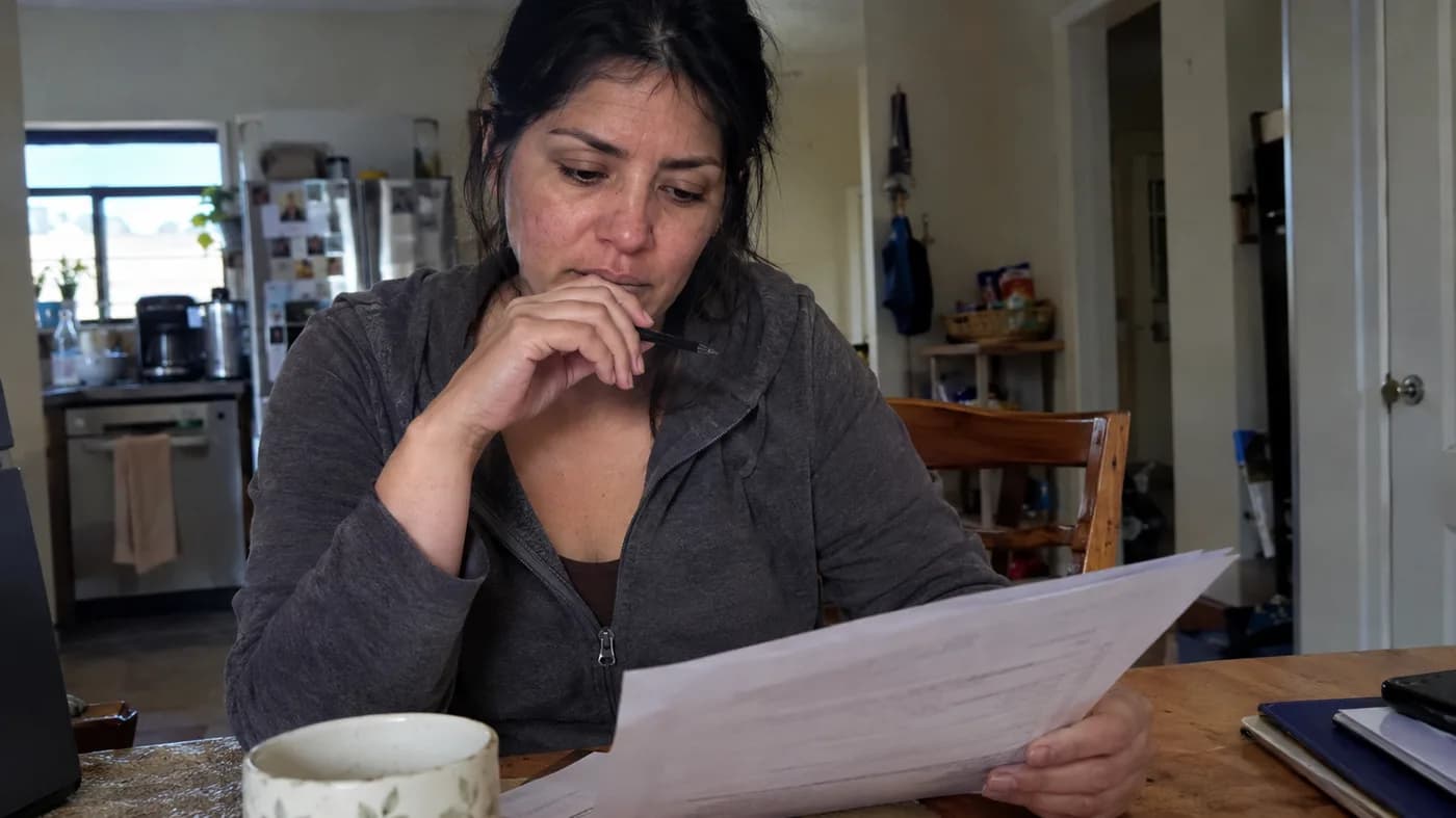 A woman in her mid-thirties reading lab results at a kitchen table with a pen