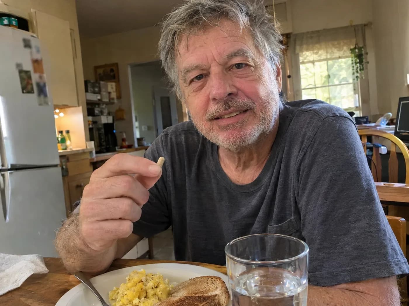 A man in his sixties taking a capsule with breakfast at his kitchen table